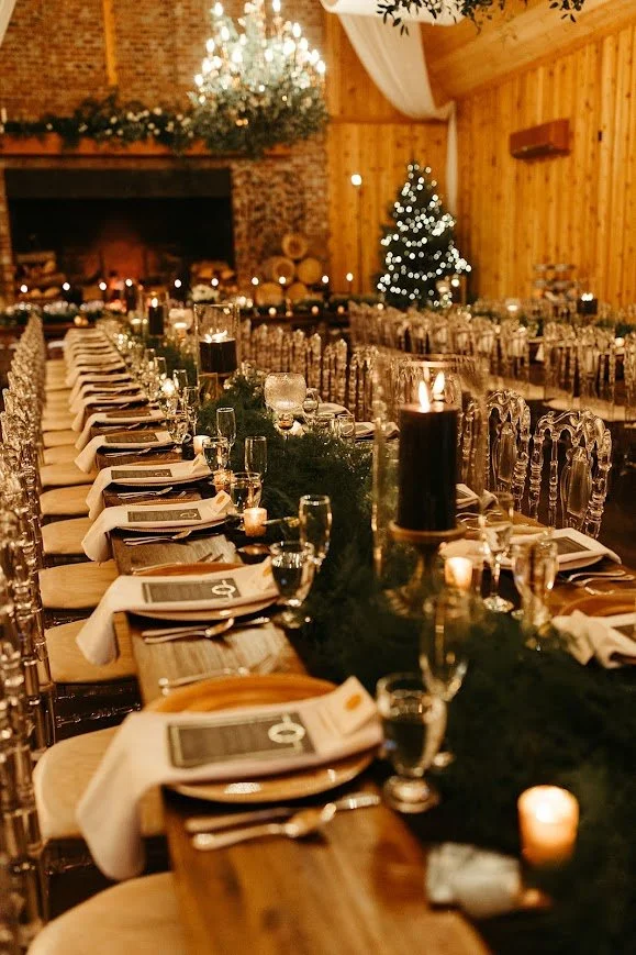 Wedding reception table with black candles and greenery near a stone fireplace and Christmas tree.