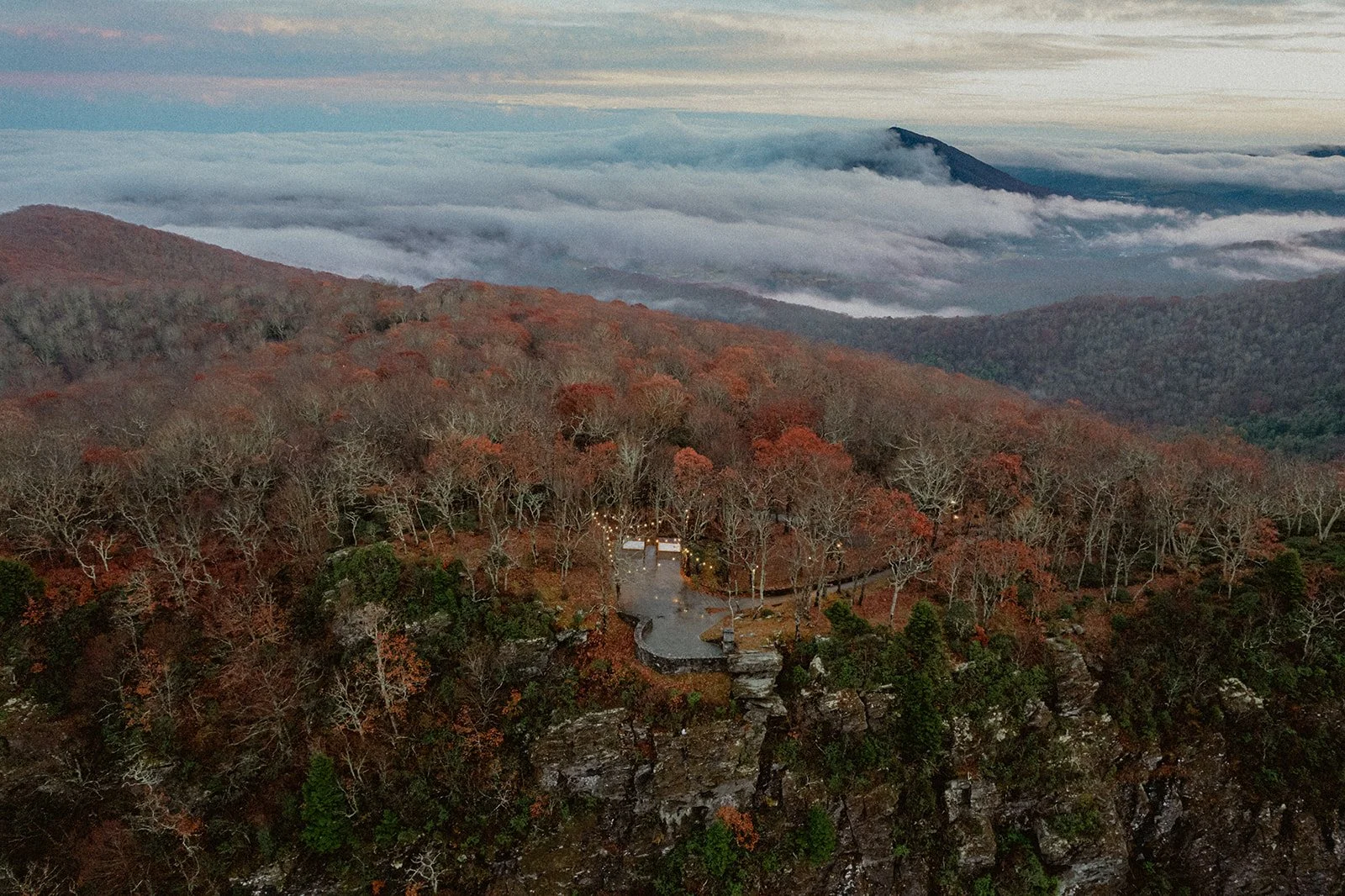 Aerial view of a mountaintop overlook ceremony site surrounded by fall-colored trees with clouds in the valleys below