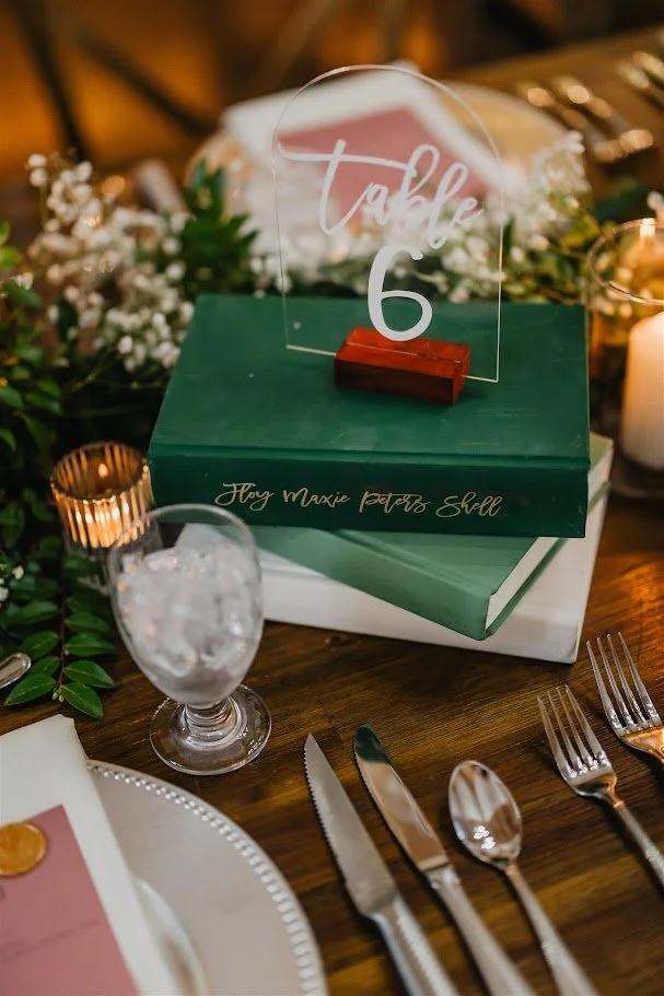 Reception table detail with table number 6 on stacked books, candles, and greenery