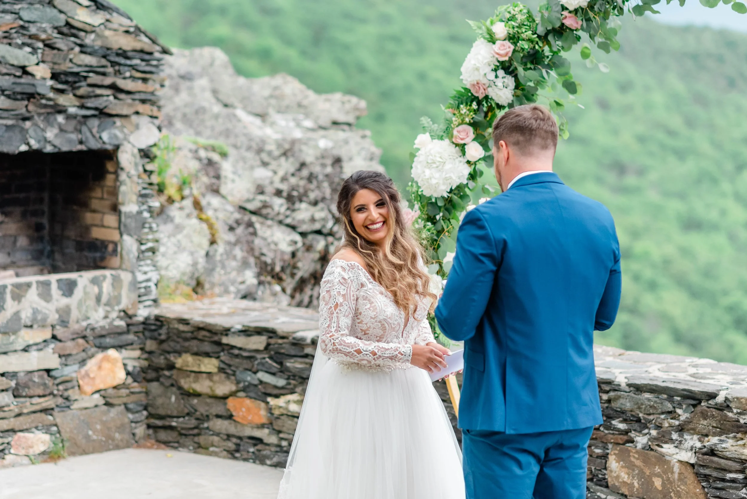 Bride smiling during a mountain wedding first look with the groom near a floral ceremony arch.