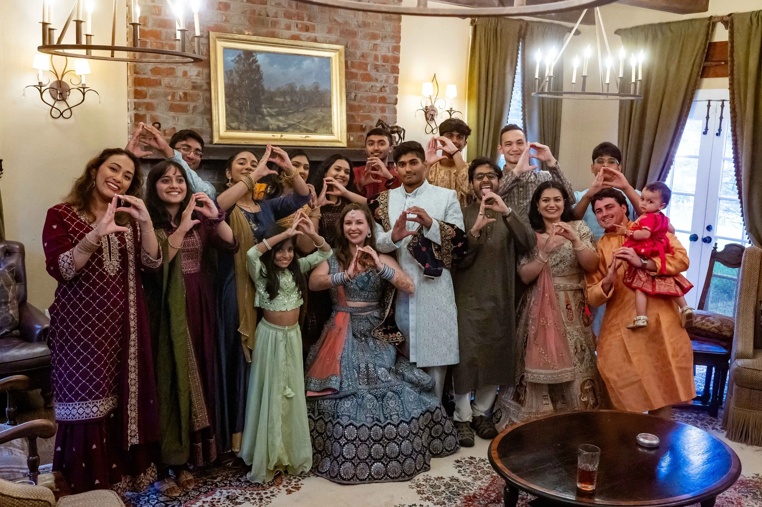 Large group posing indoors during an Indian wedding celebration, making heart shapes with their hands