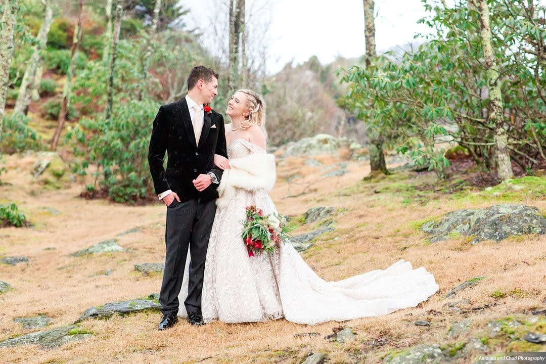Bride and groom standing together outdoors in a winter forest clearing, bride in a fur wrap.