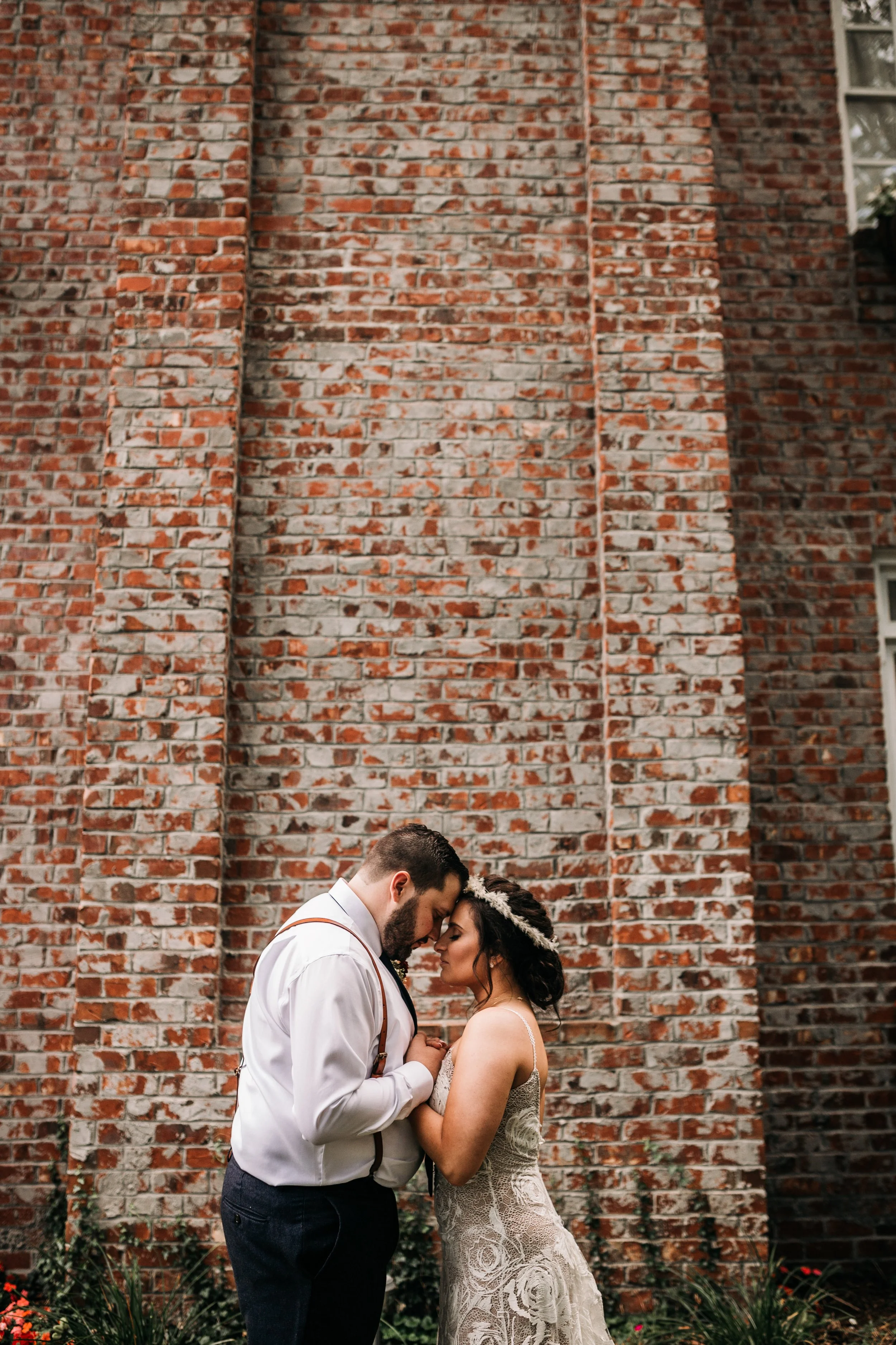 Intimate wedding portrait of the couple touching foreheads in front of a textured brick wall.