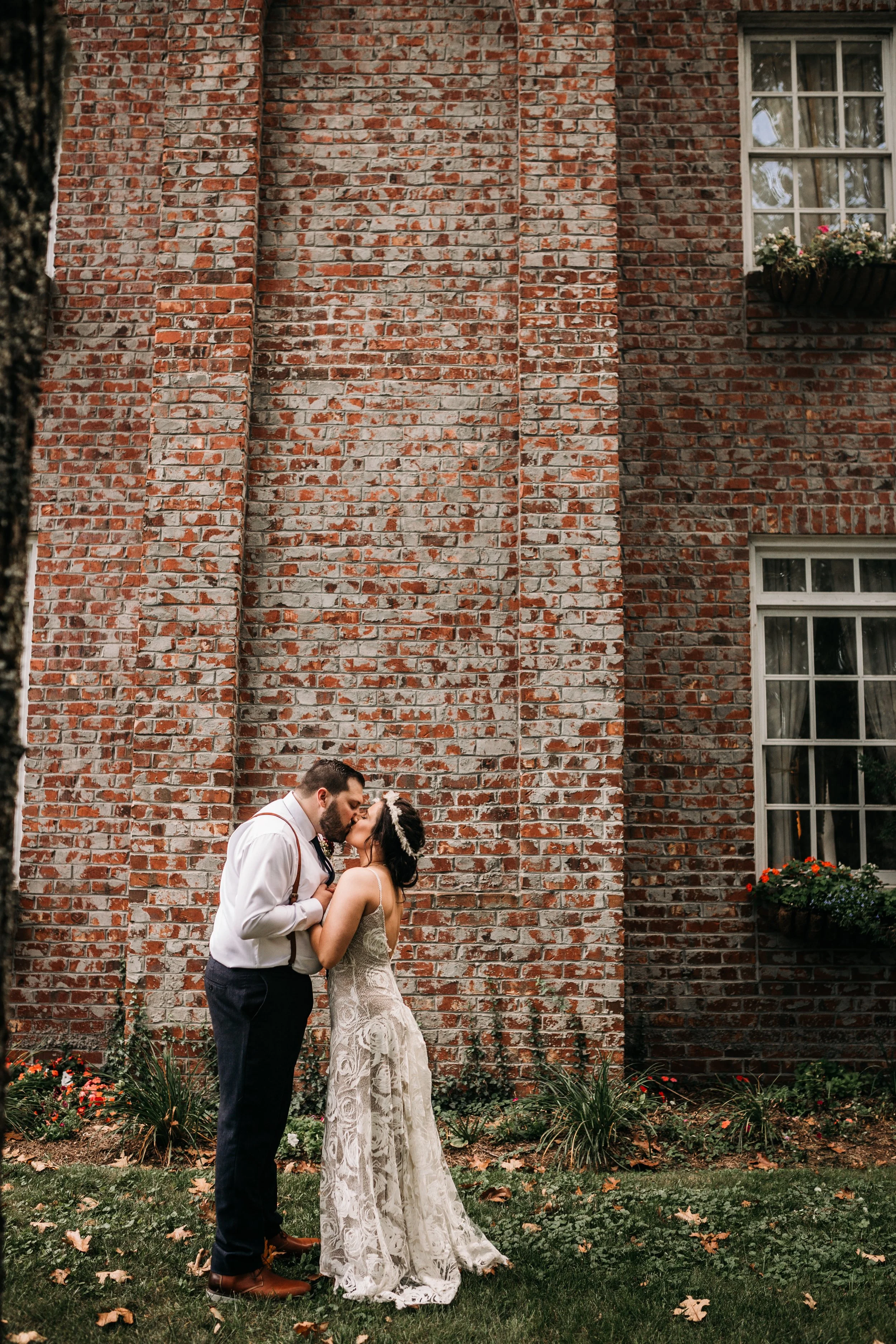 Bride and groom kissing in front of a tall brick wall for a rustic urban portrait.
