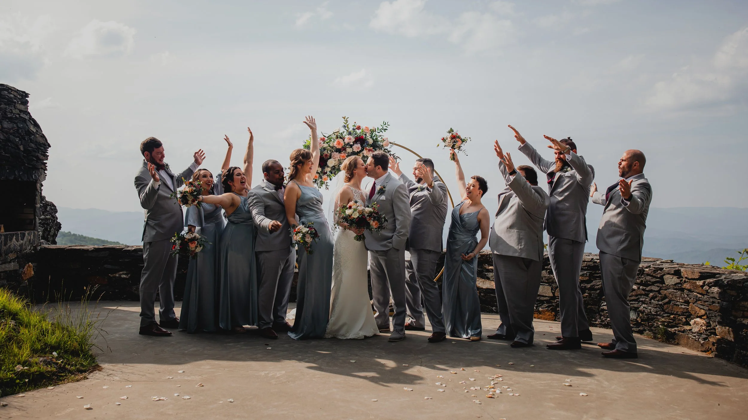 Wedding party celebrating around the bride and groom at a mountain ceremony with a floral arch and expansive views