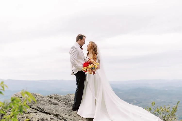 Bride and groom standing on a mountain cliff with scenic views during their wedding portrait.