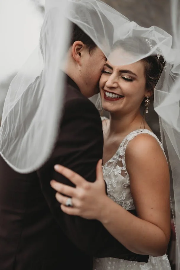 Bride and groom laughing together under the wedding veil during a romantic close-up portrait.
