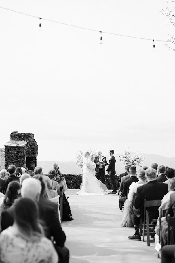 Wide shot of a mountaintop wedding ceremony with guests seated and string lights overhead