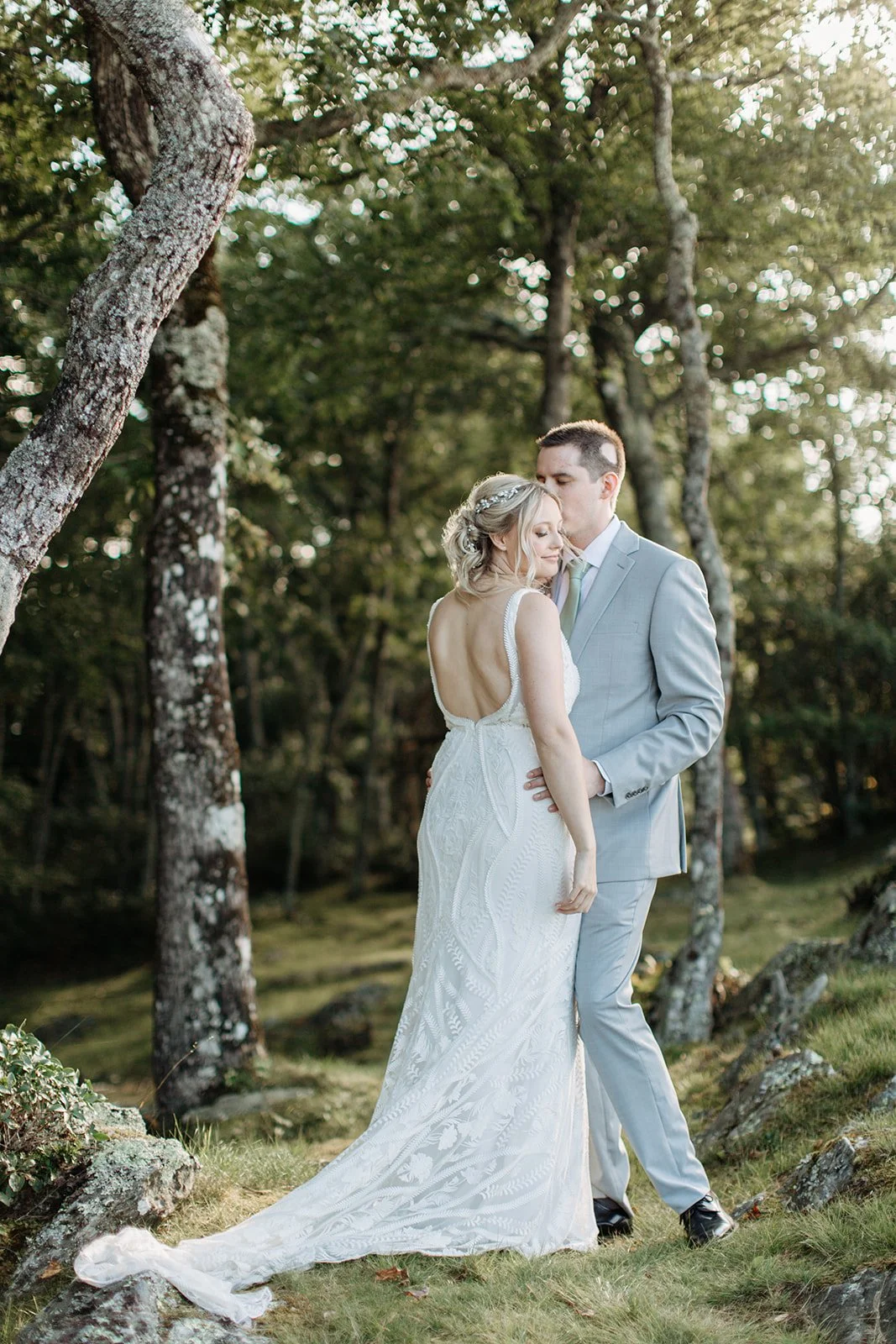 Bride and groom embracing in a romantic woodland wedding portrait with the groom in a light gray suit.