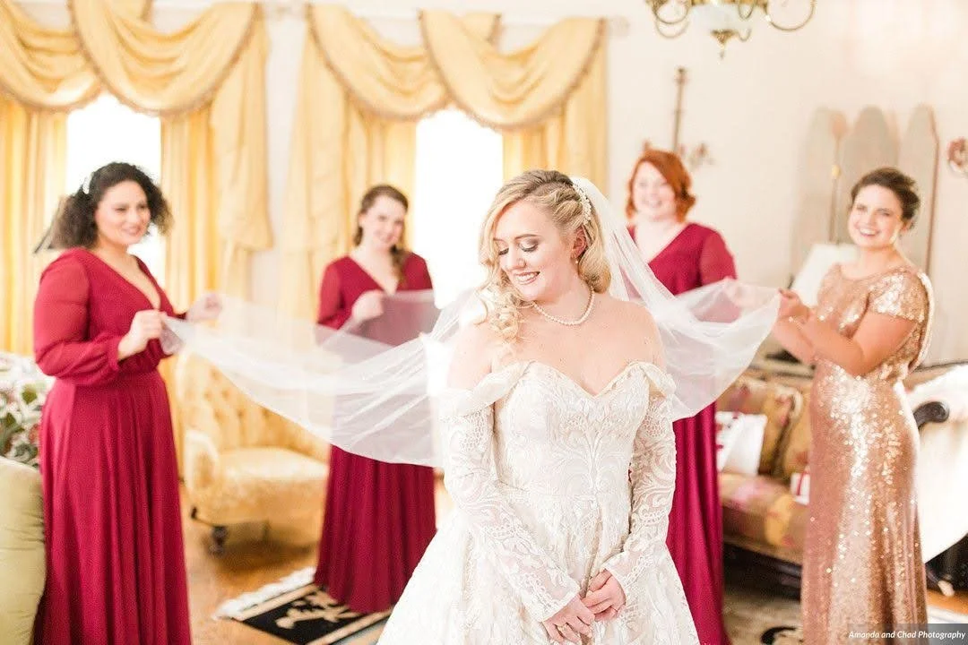 Bride smiling as her veil is lifted while bridesmaids stand behind her during getting ready.