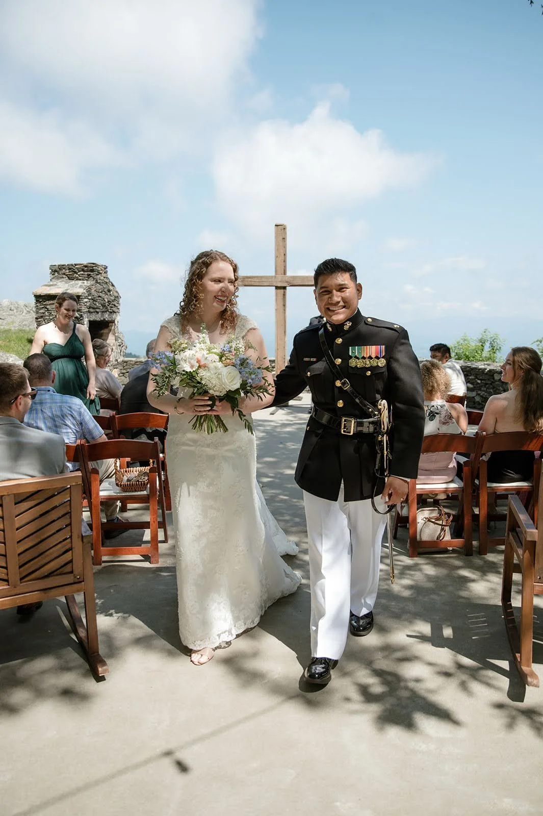 Newlyweds walking down the aisle after a mountain overlook ceremony with a wooden cross behind them.