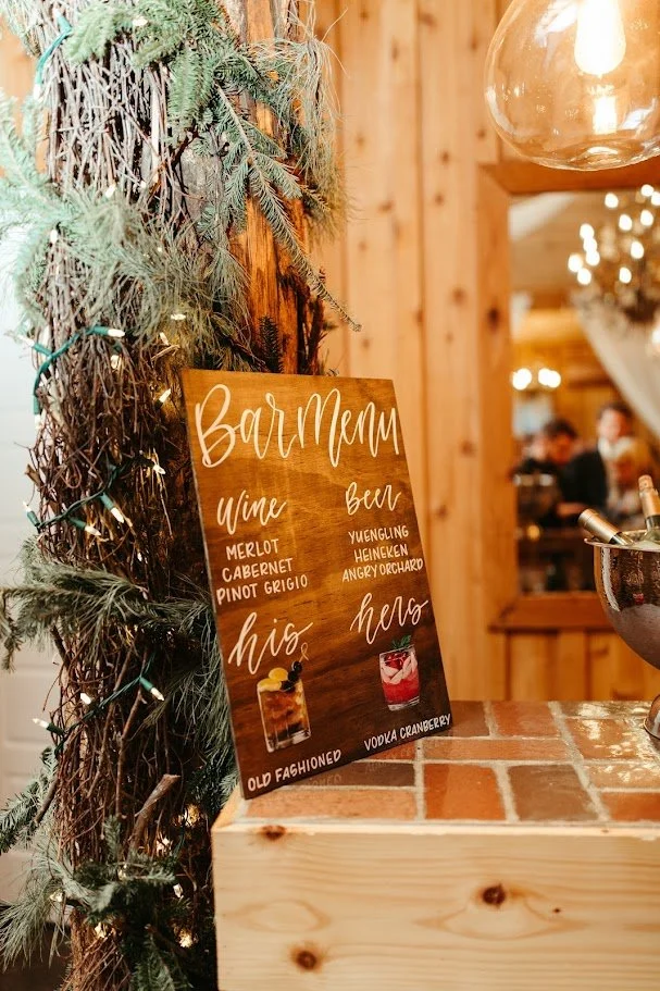 Rustic wedding welcome sign decorated with greenery and warm floral accents near the venue entrance.