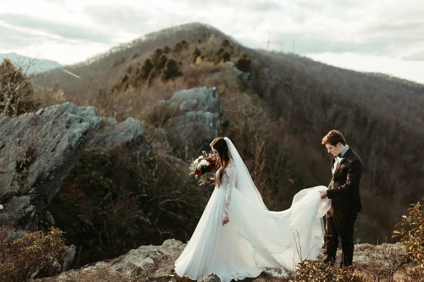 Bride and groom standing on rocky mountain terrain with the bride’s veil flowing behind her.