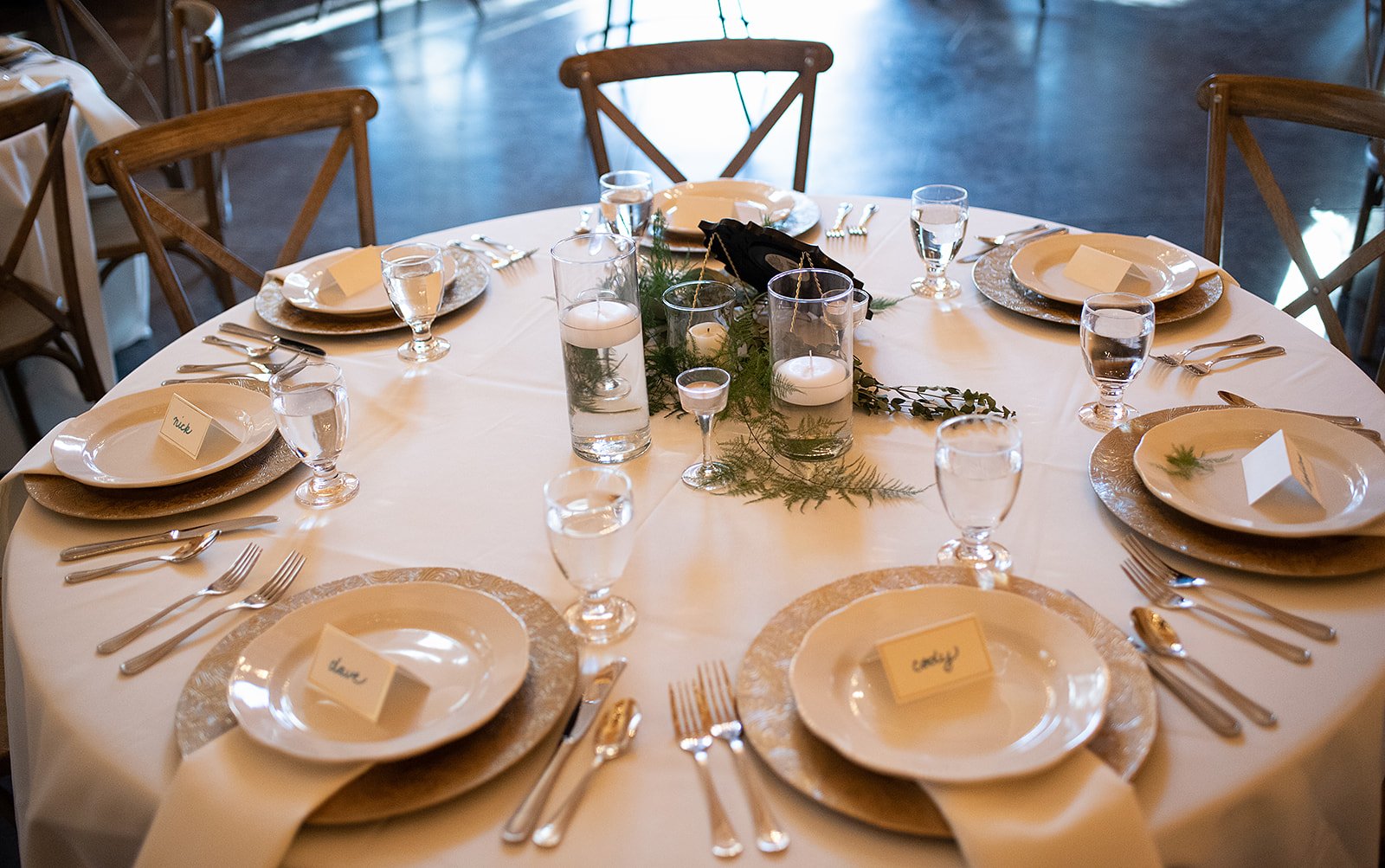 Round reception table with place settings, greenery, and glass cylinder candles as centerpieces.