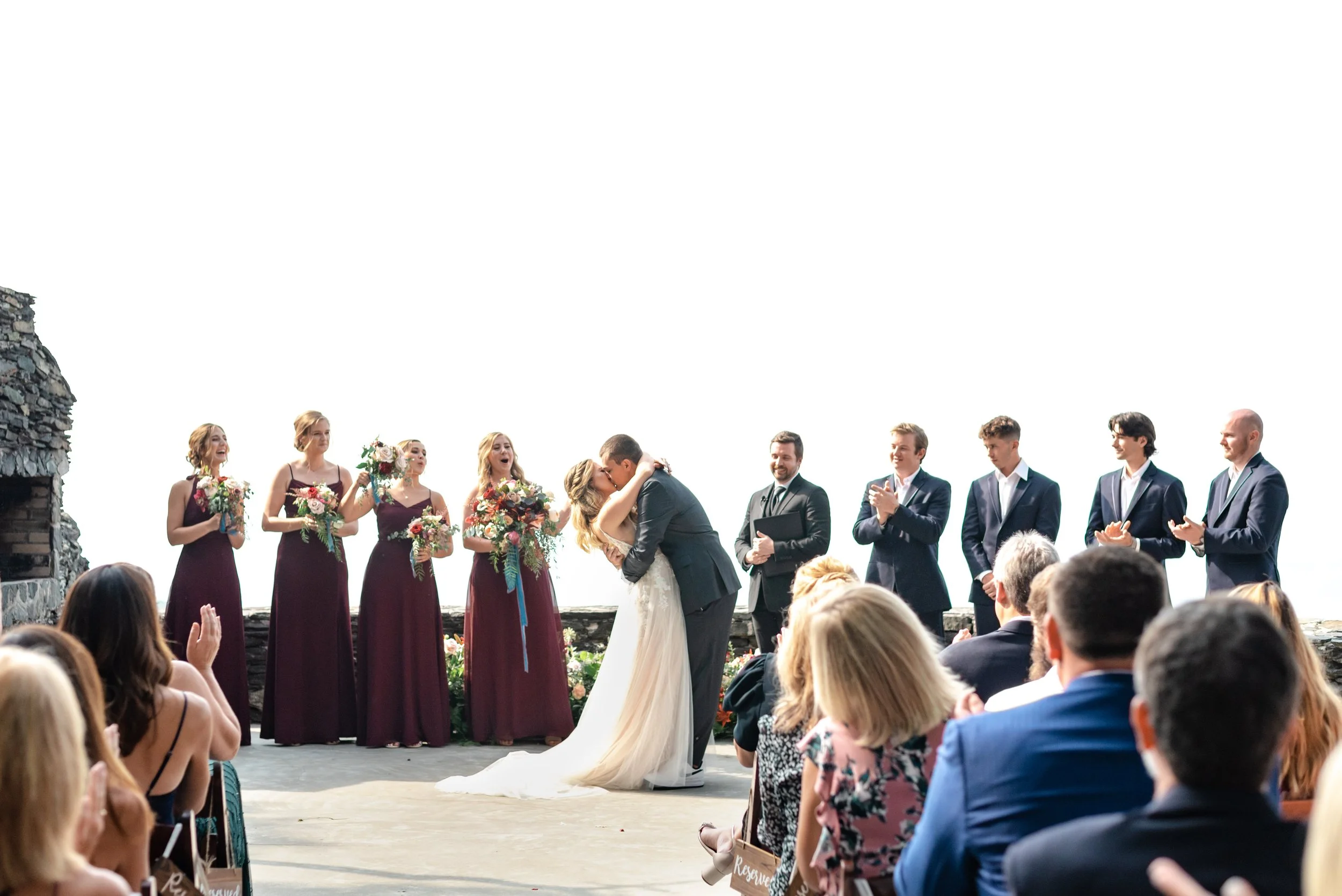 Bride and groom kissing during the ceremony as bridesmaids and groomsmen stand behind them.