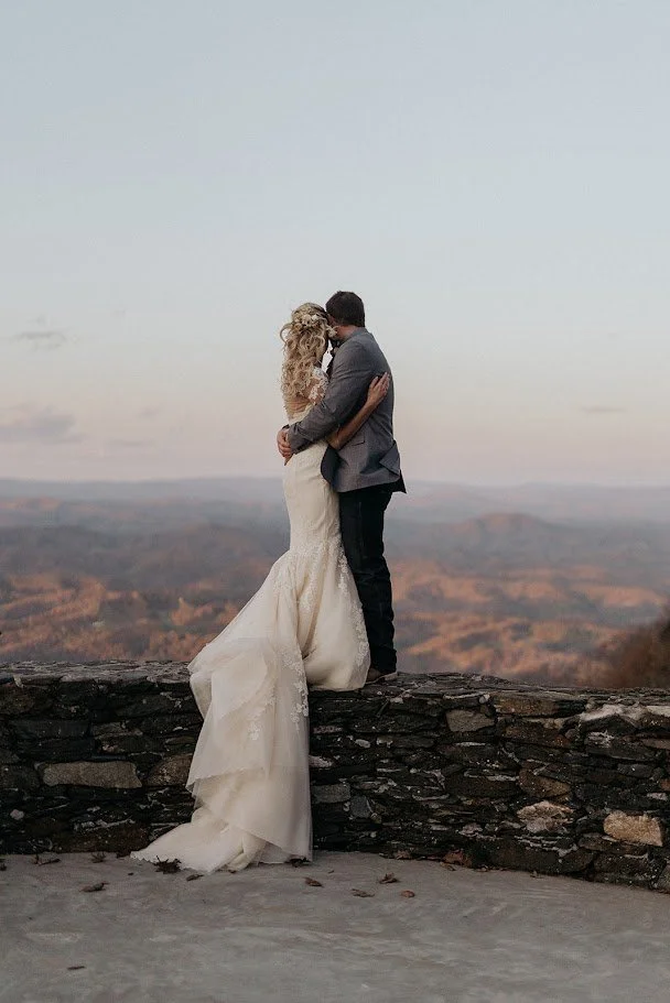 Bride and groom kissing on a mountain overlook with the bride’s long train flowing behind