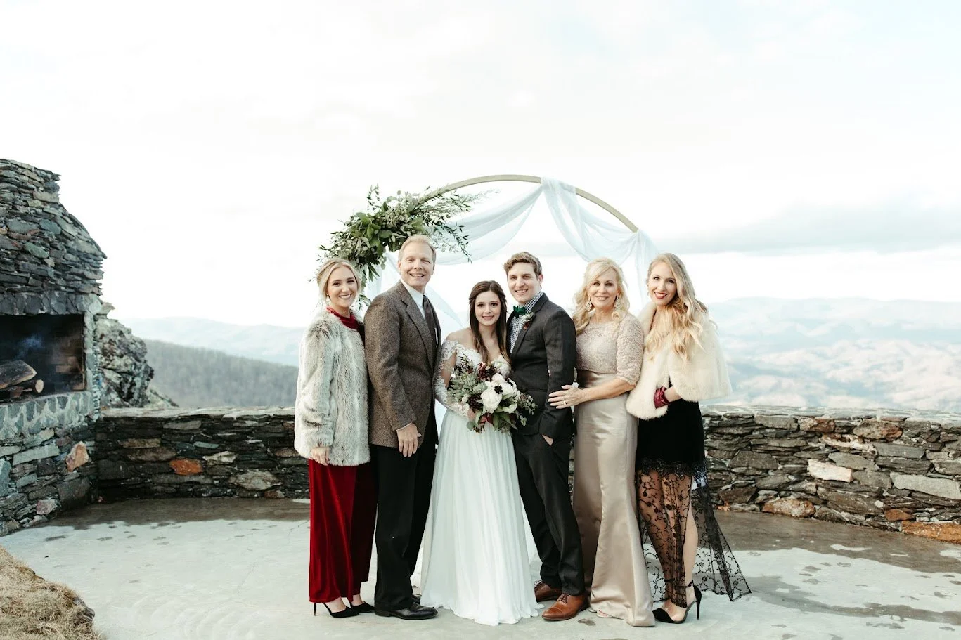 Intimate mountain overlook wedding ceremony with couple, officiant, and family beneath a circular arch.