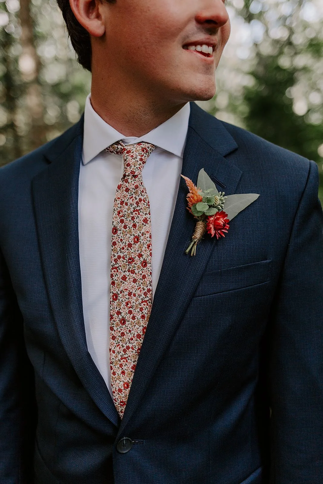 Groom wearing a navy suit with a floral tie and boutonniere for a wedding day detail portrait.
