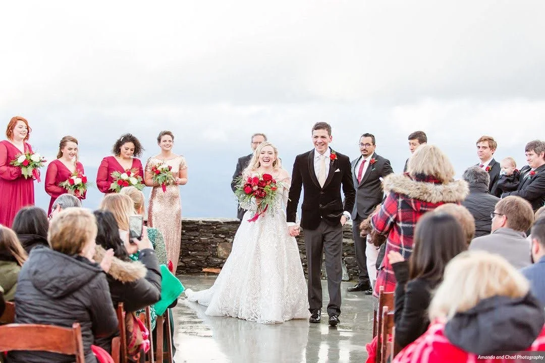 Bride and groom walking down the aisle after an outdoor ceremony at a mountain overlook as guests applaud.