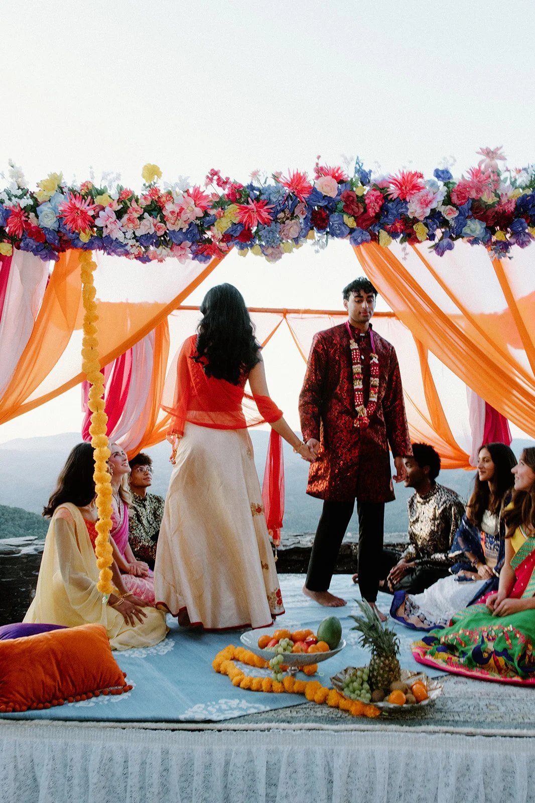 Indian couple walking together on a stone terrace at sunset with a decorated mandap behind them