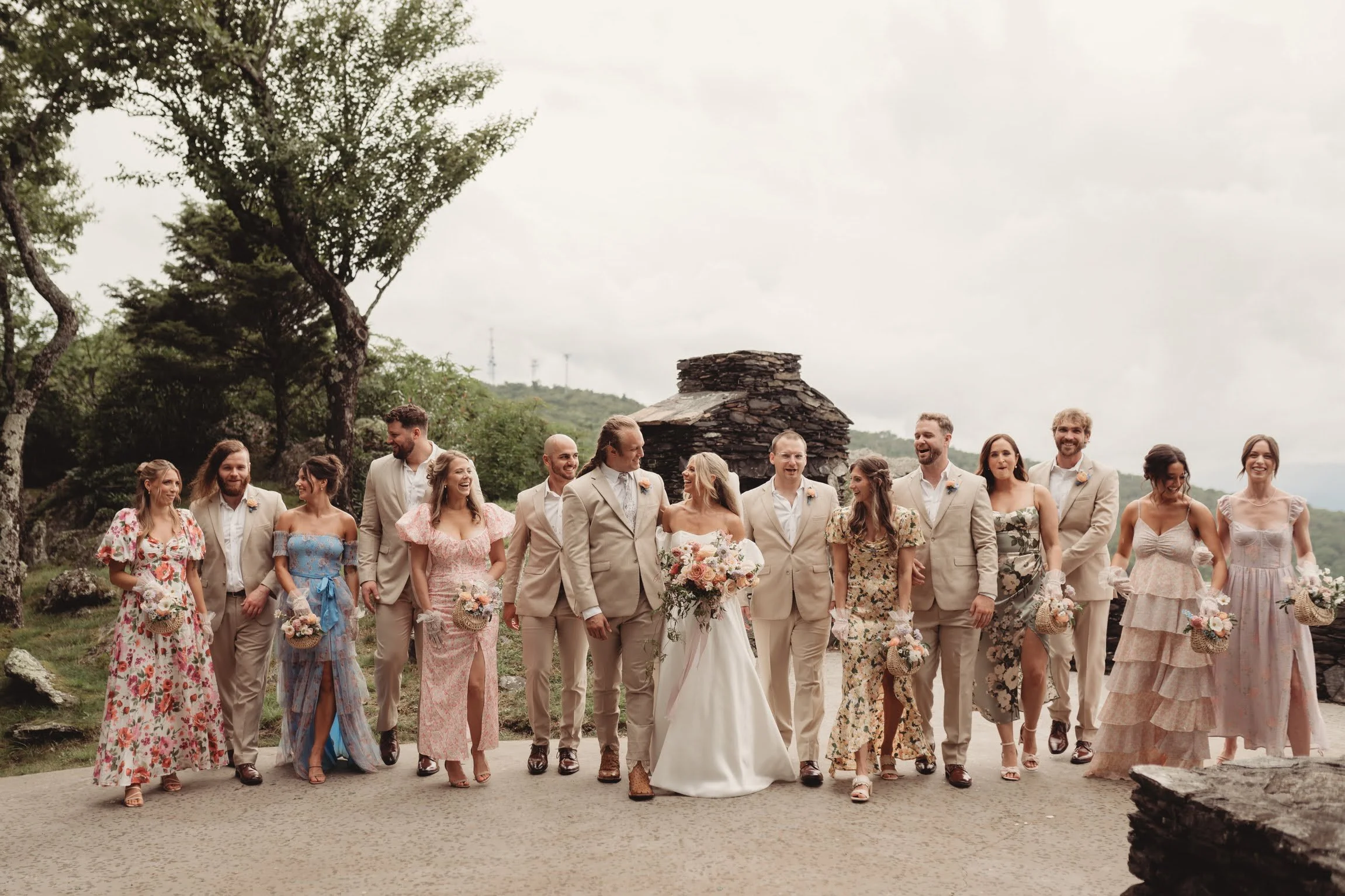 Large wedding party group photo outdoors with the bride and groom surrounded by attendants in neutral-toned outfits.