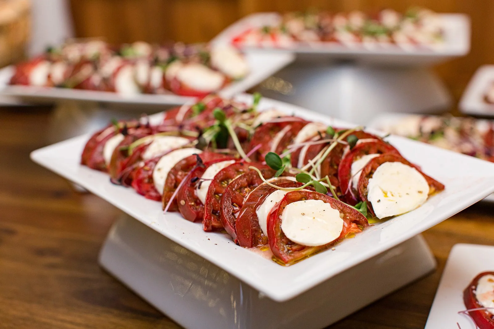 Caprese salad platter with sliced tomatoes, fresh mozzarella, herbs, and balsamic drizzle served on a white tray for wedding cocktail hour.