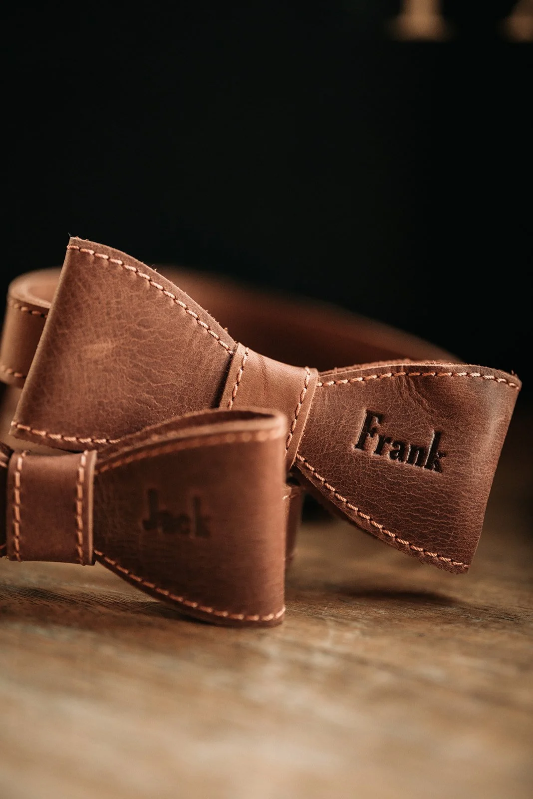 Personalized brown leather bow tie detail engraved with the name Frank for a rustic wedding.