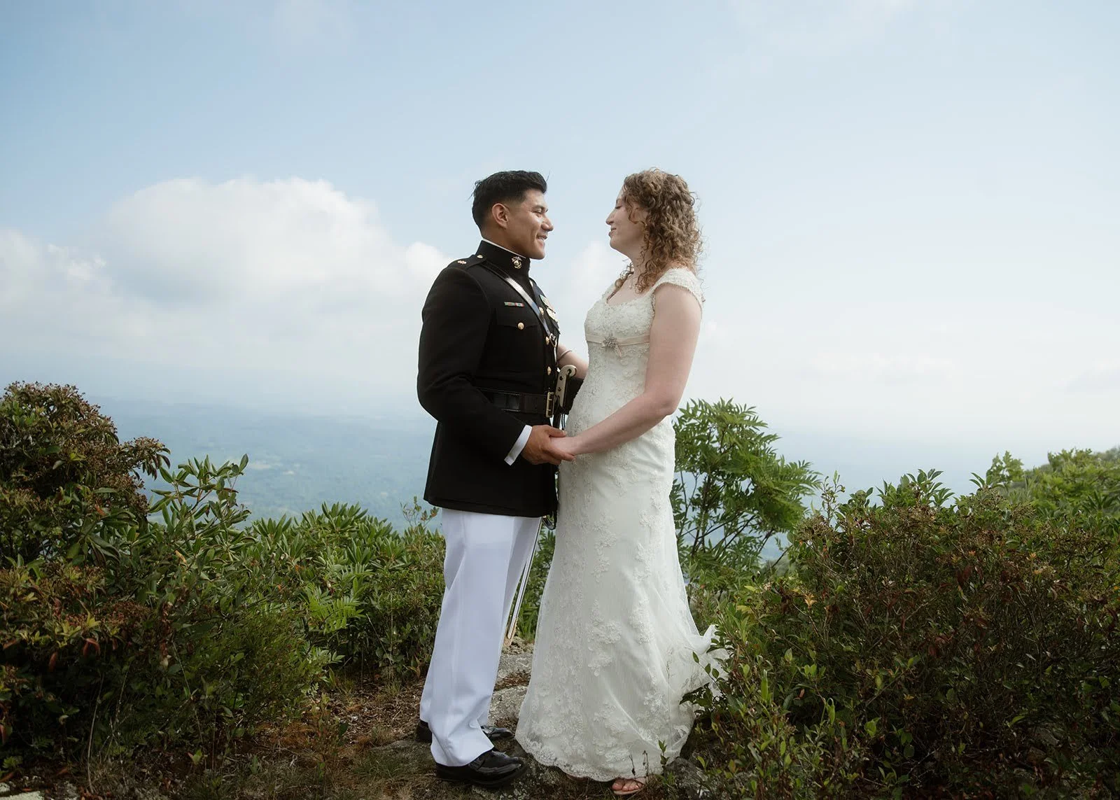 Bride and military groom holding hands for a romantic portrait at a misty mountain overlook.