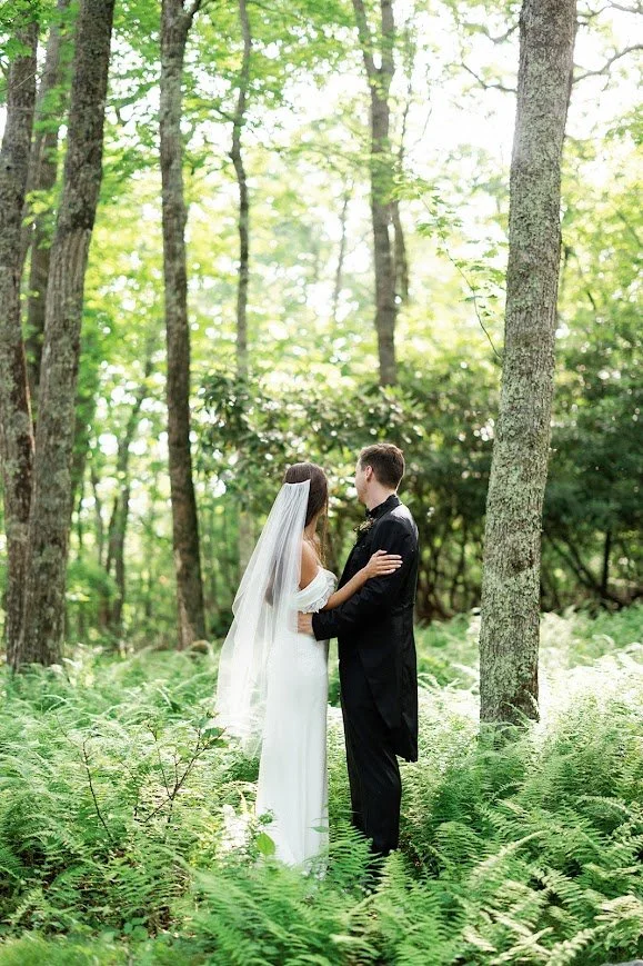 Bride and groom standing together in a fern-filled forest for wedding portraits.