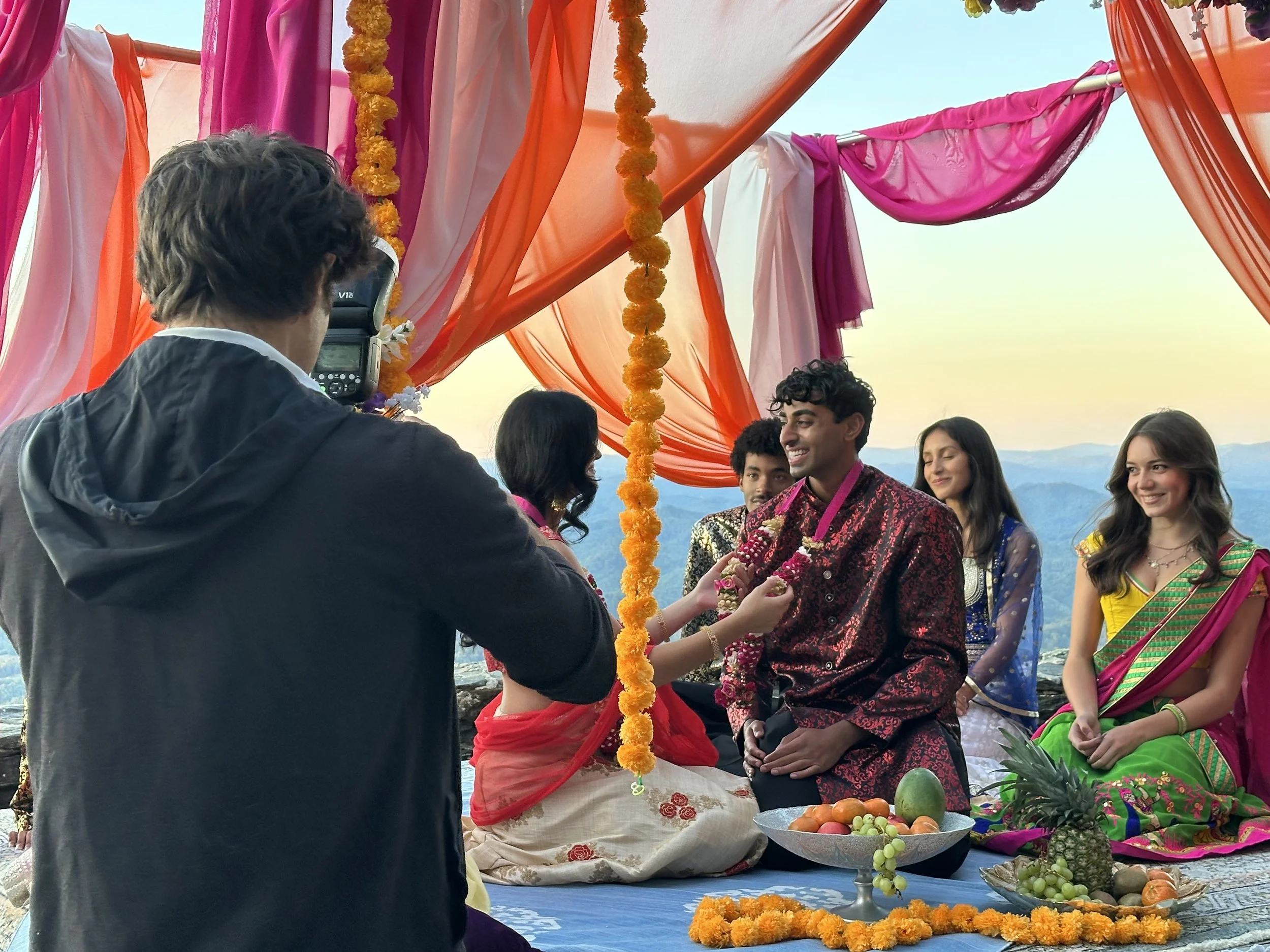 Indian wedding ceremony moment under a colorful mandap with guests seated and mountains in the background