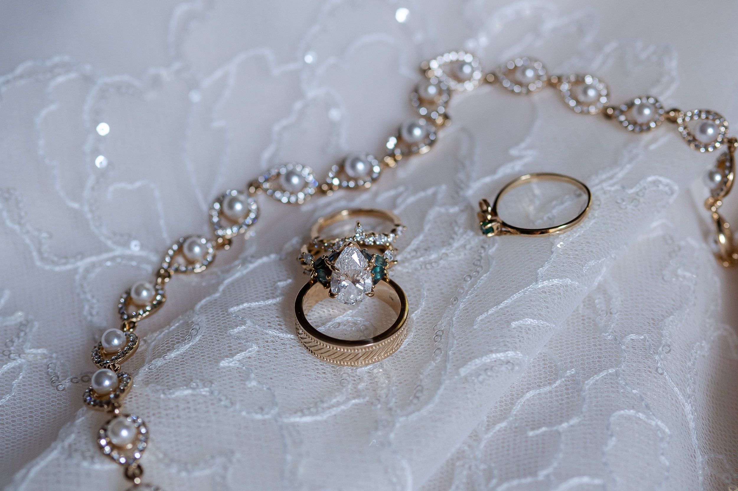 Wedding rings and pearl bracelet displayed on white lace fabric for bridal detail photos.