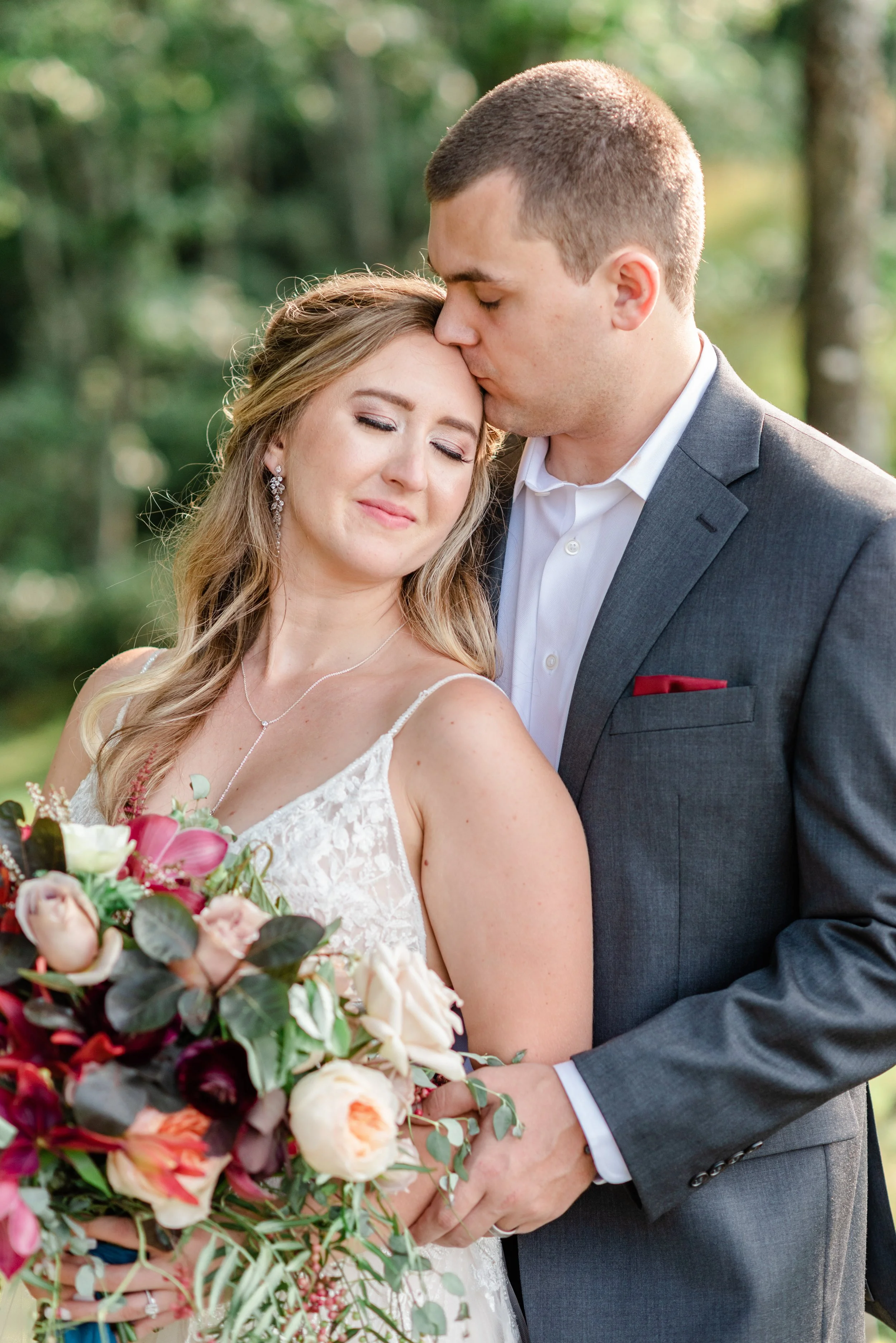 Groom kissing the bride’s forehead during a romantic portrait with bouquet in the foreground.