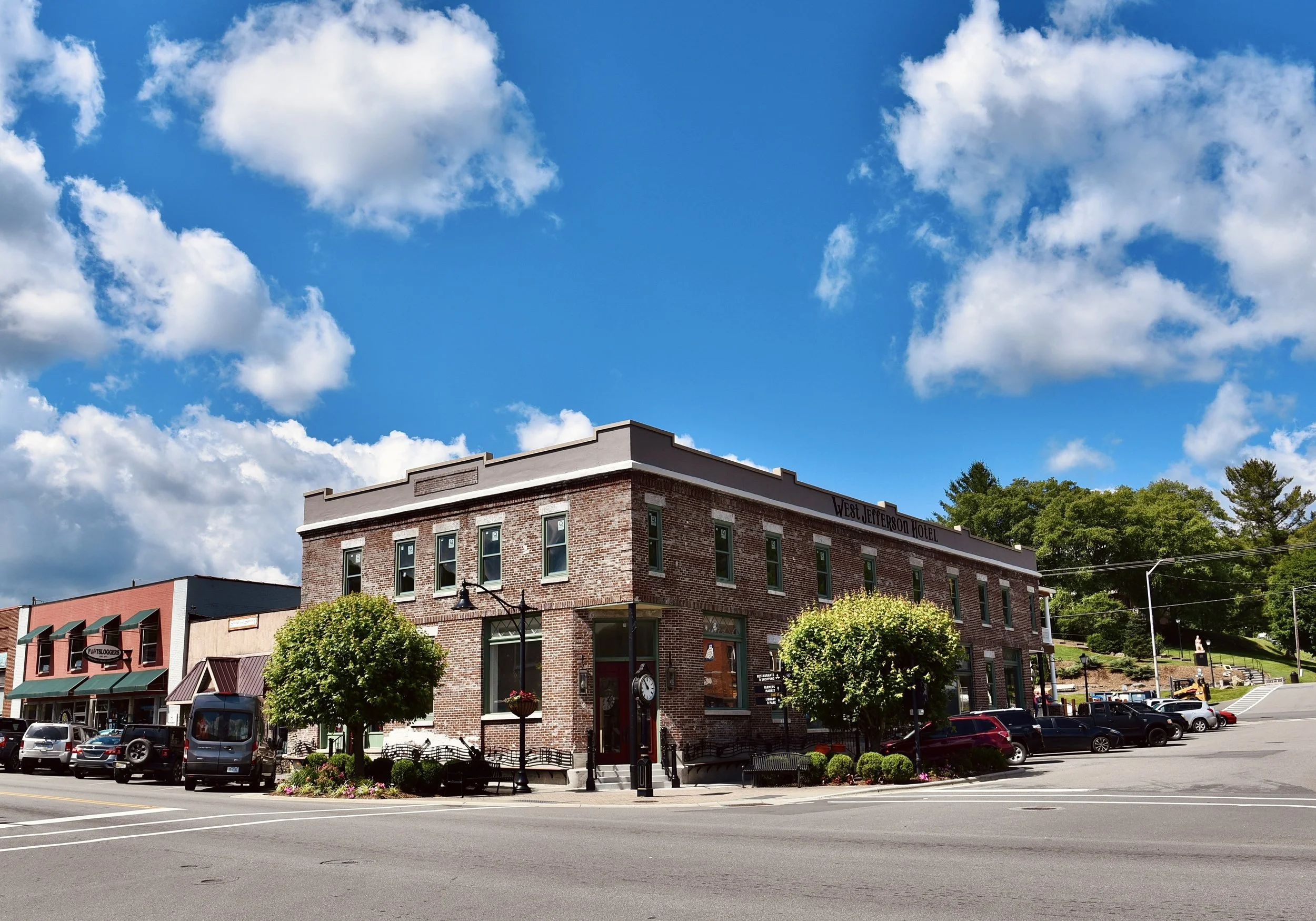 Restored brick hotel building on a street corner under a bright blue sky with scattered clouds.