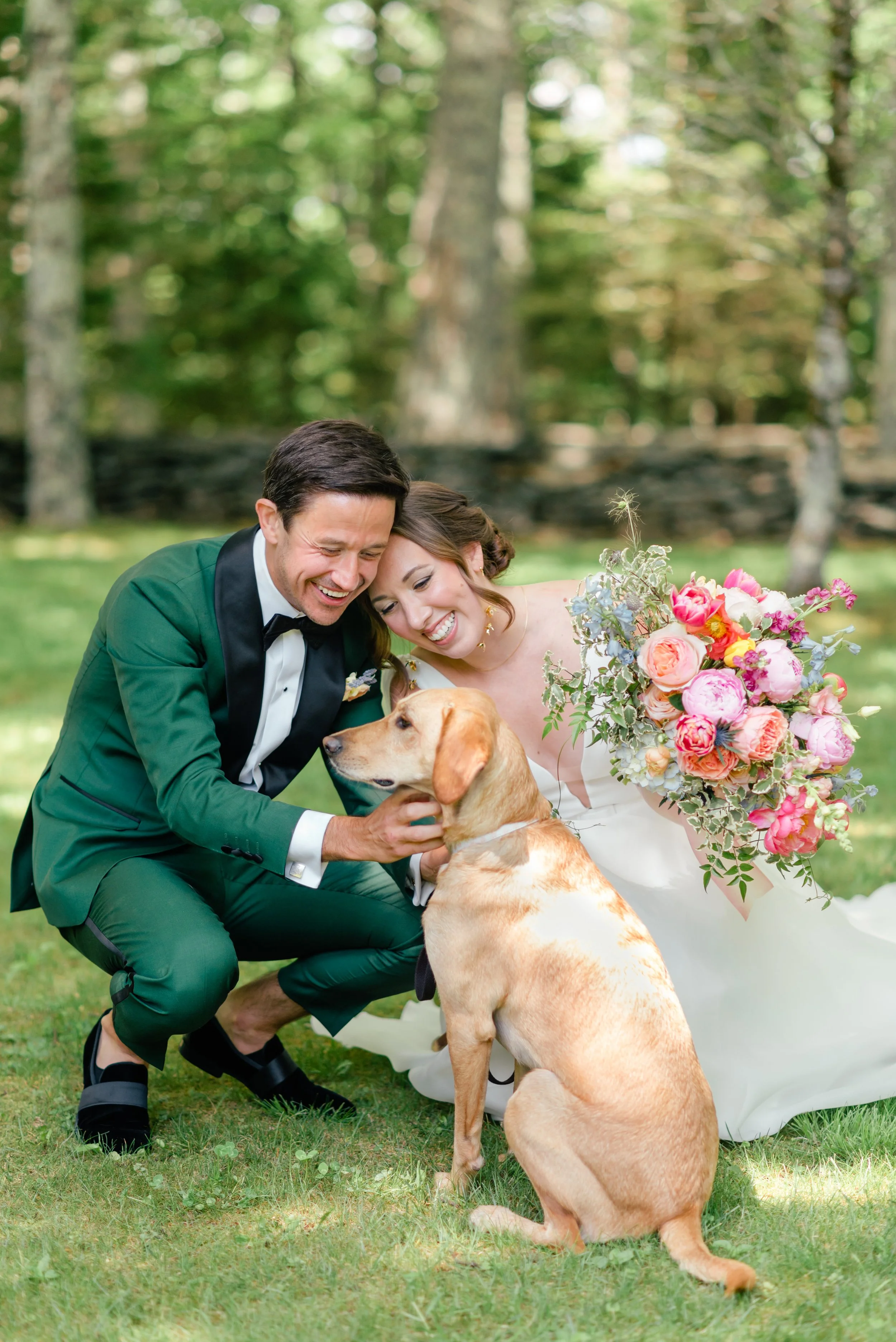 Bride and groom posing with their dog outdoors while holding a bright colorful wedding bouquet.
