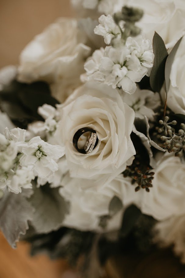 Wedding rings nestled inside a white rose bouquet with soft floral details.