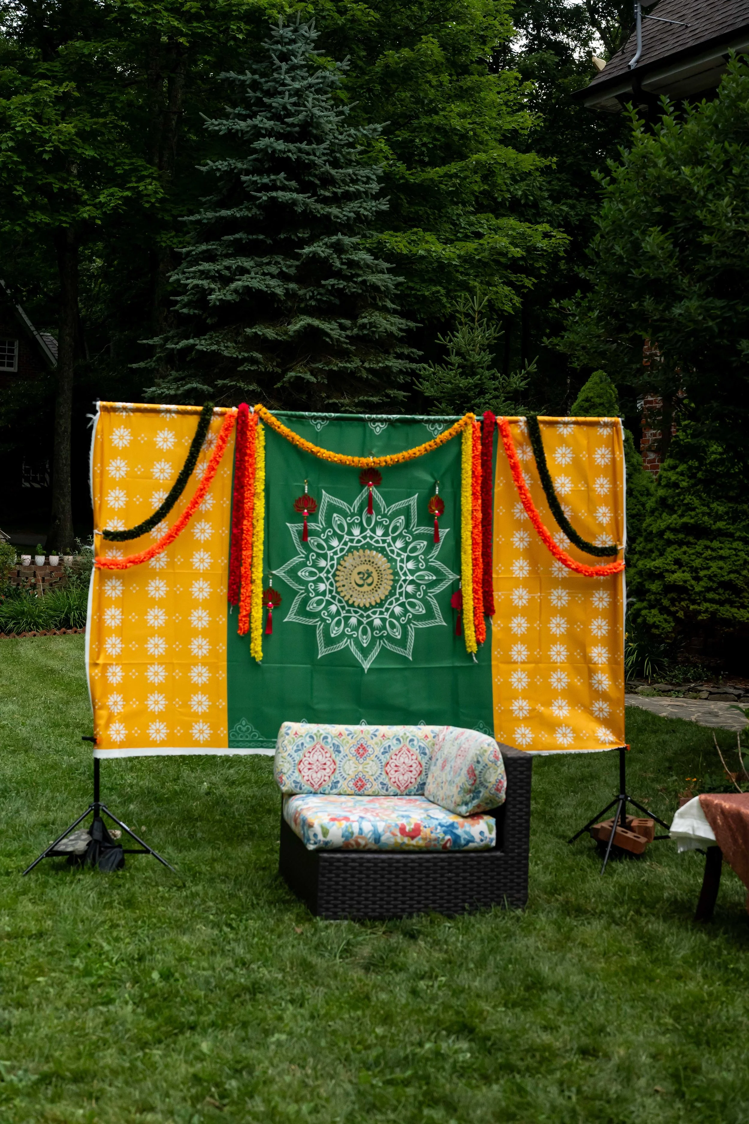 Colorful Indian wedding backdrop with yellow and green fabric, marigold garlands, mandala design, and lounge chair.