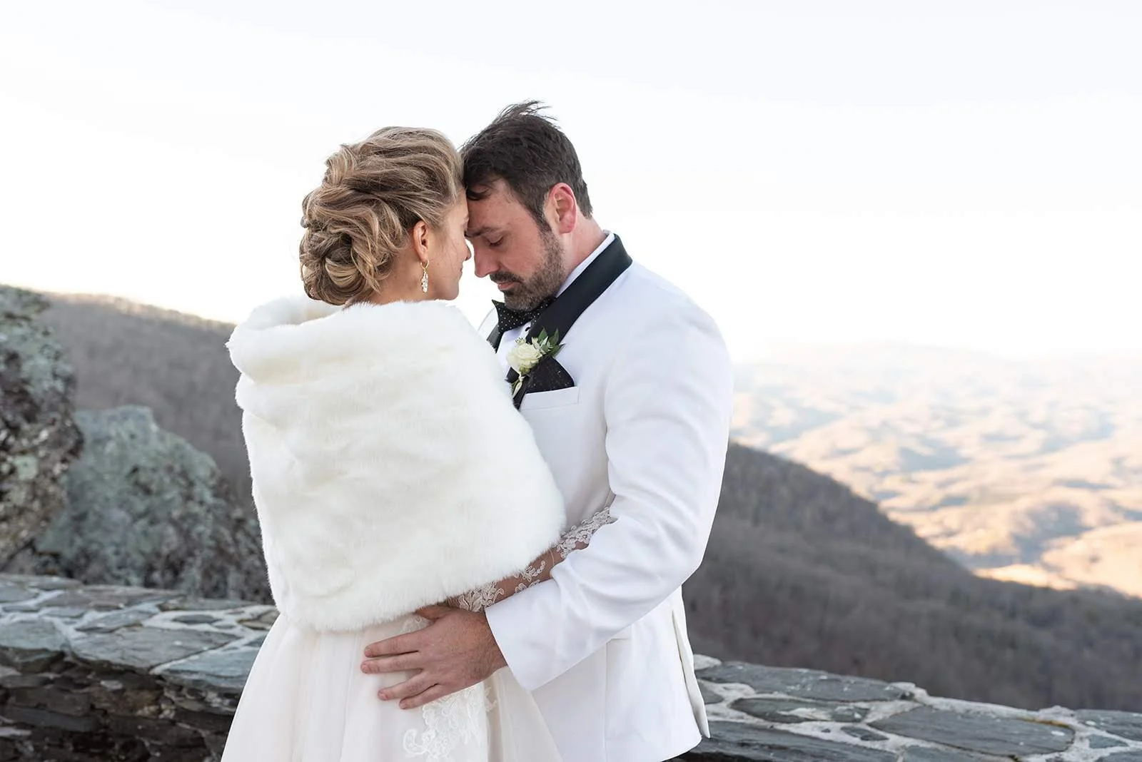 Bride and groom embracing on a winter mountain overlook, bride wearing a fur wrap.