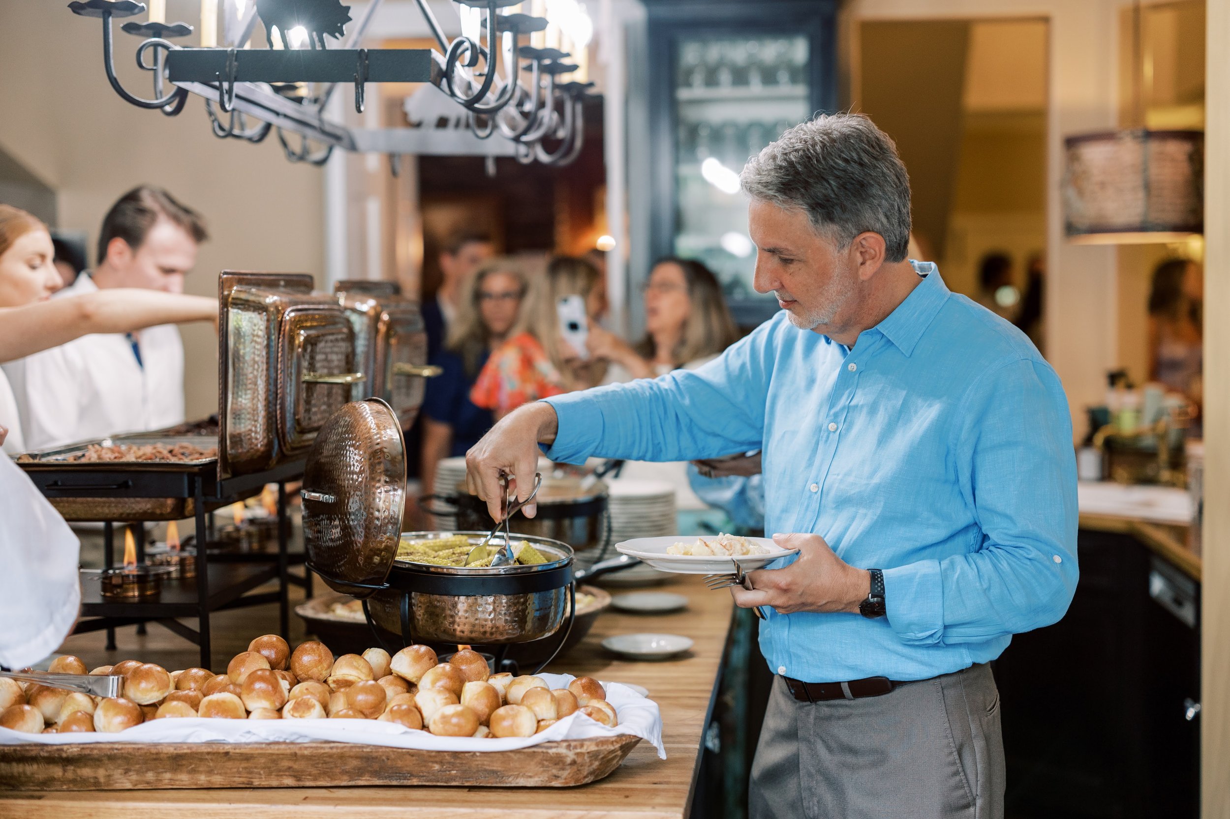 Caterer serving food at a corporate retreat buffet station with appetizers and warm indoor event lighting.