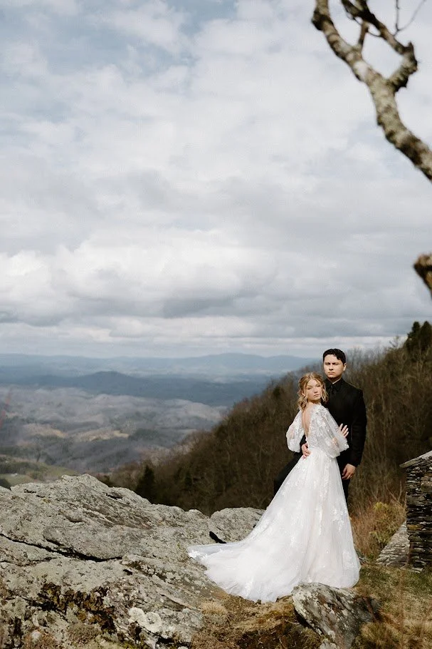Bride and groom posing on a rocky mountain overlook under a dramatic cloudy sky