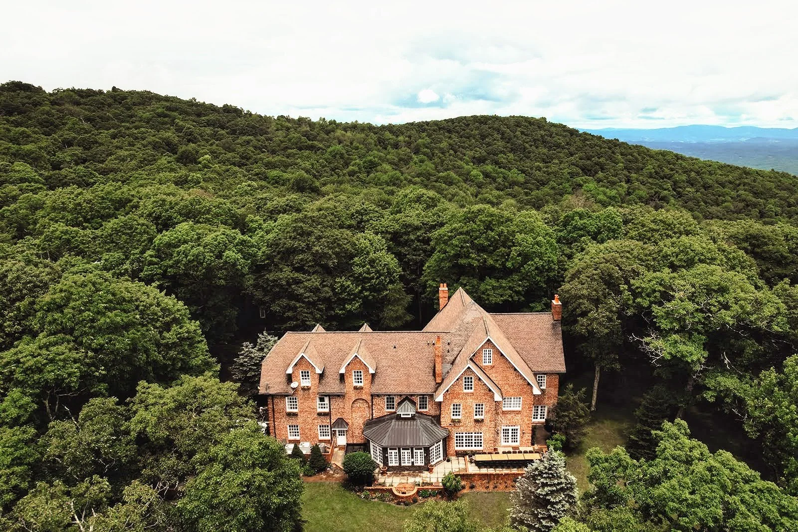 Aerial view of a brick estate wedding venue surrounded by dense green forest