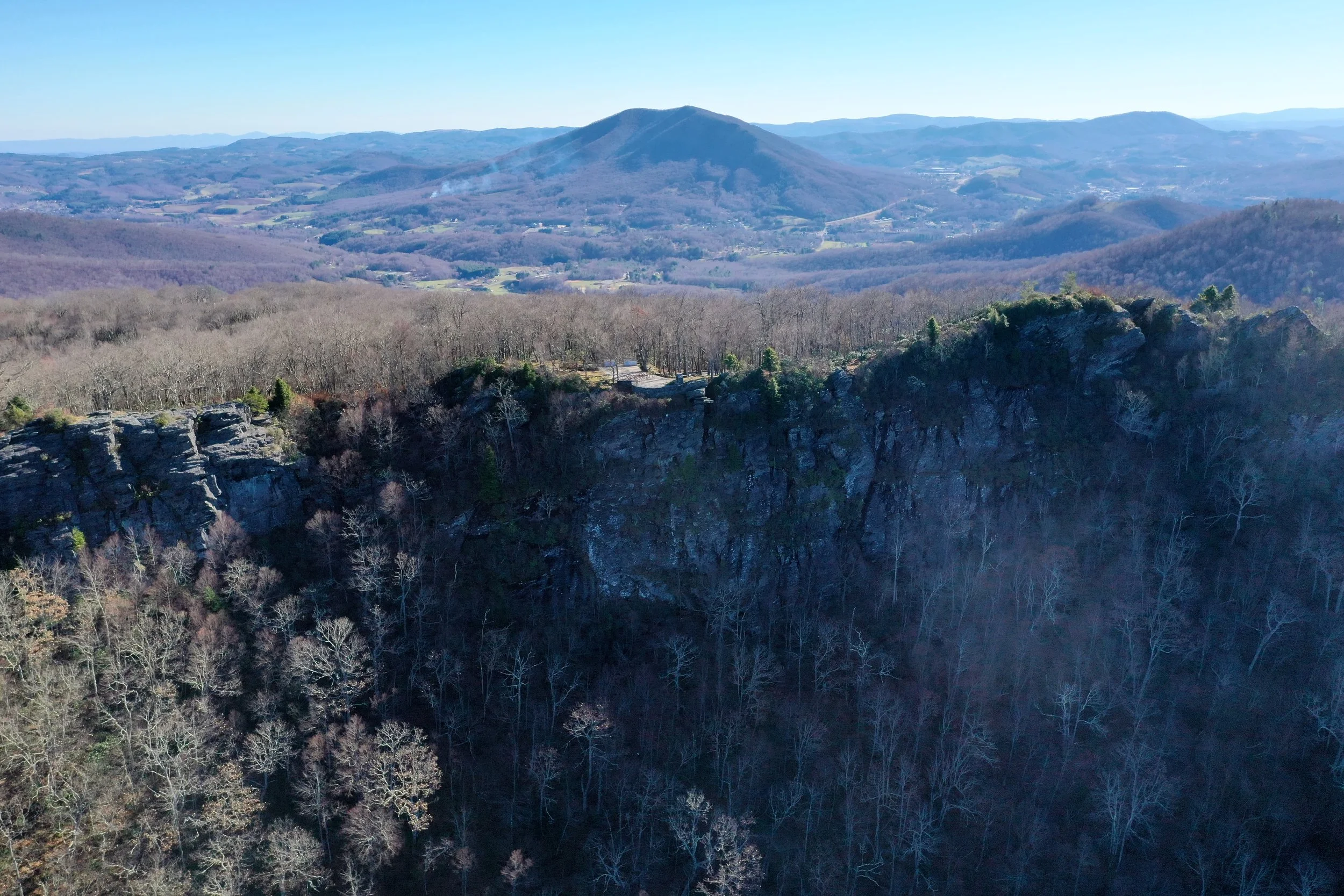 Aerial view of a steep cliffline and forested mountain overlook with a wide valley and distant ridges