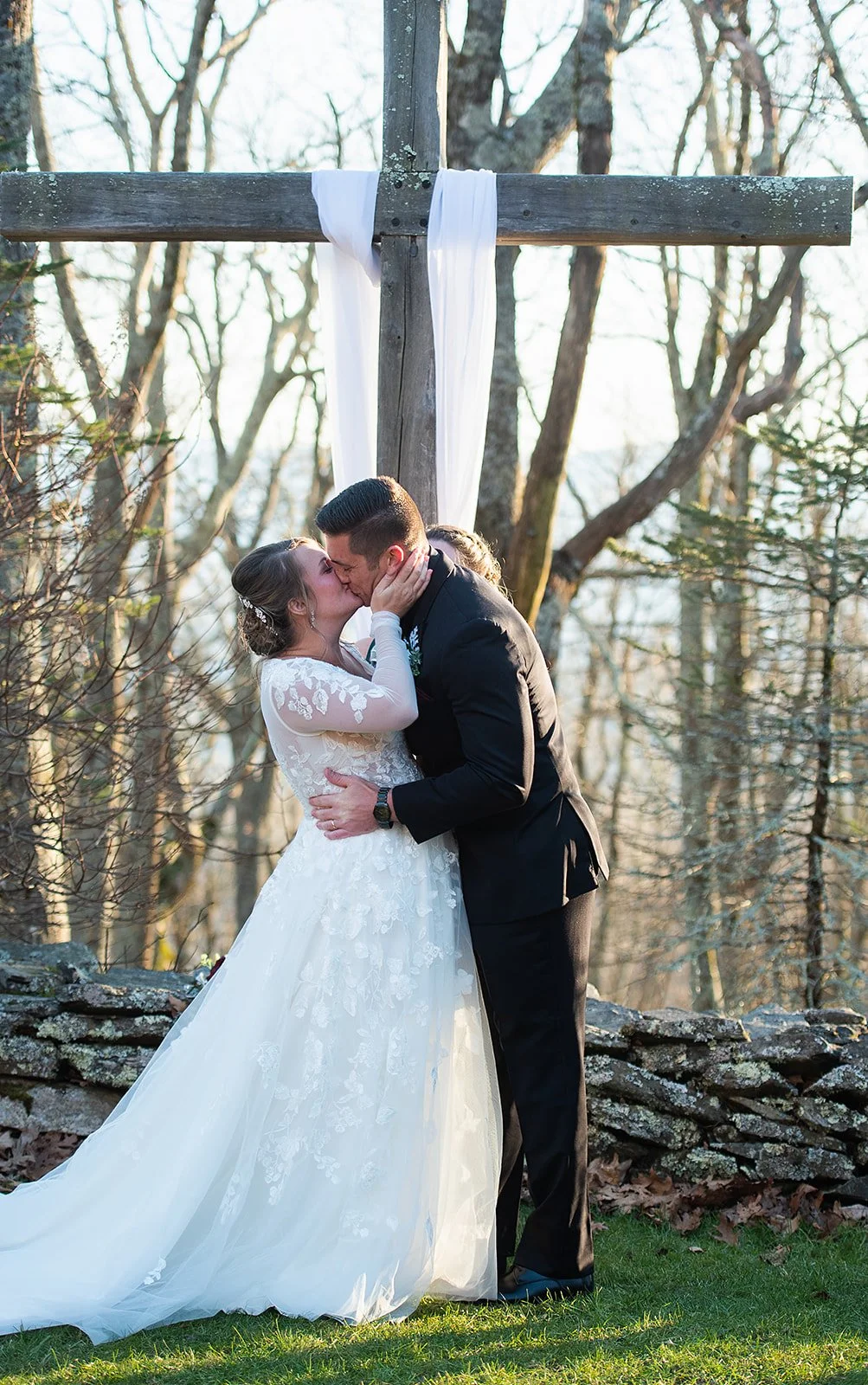 Bride and groom kissing outdoors under a wooden arbor during the wedding ceremony.