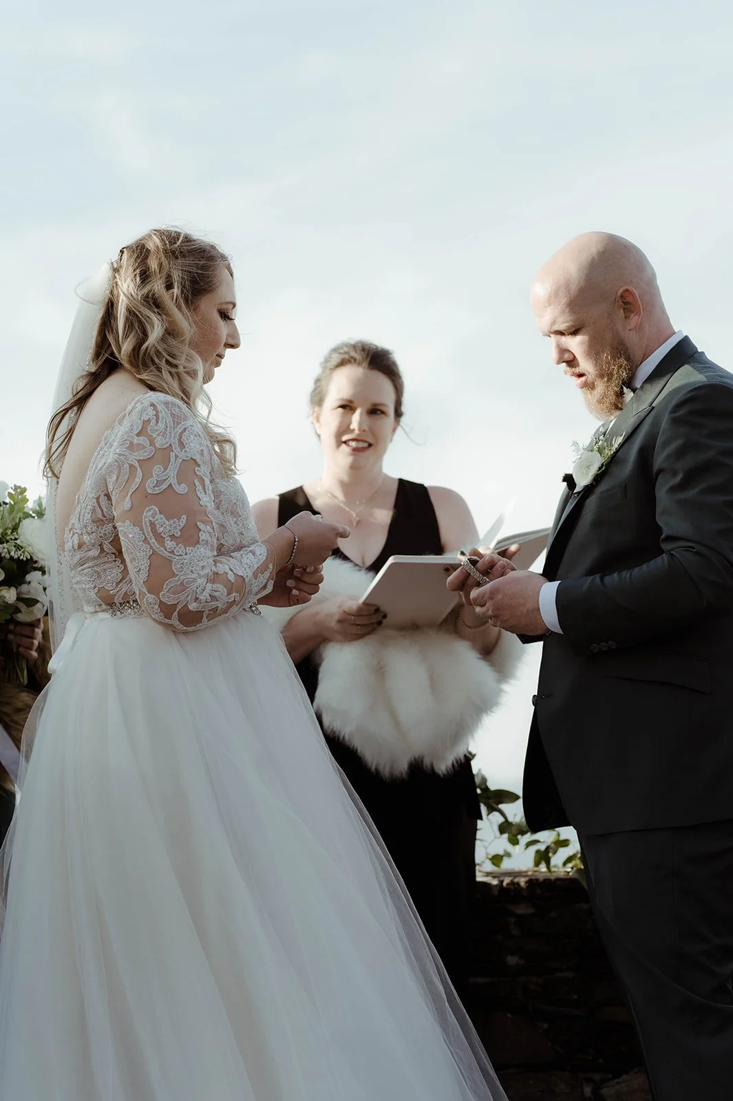 Bride and groom exchanging rings during an outdoor mountain wedding ceremony with officiant nearby.