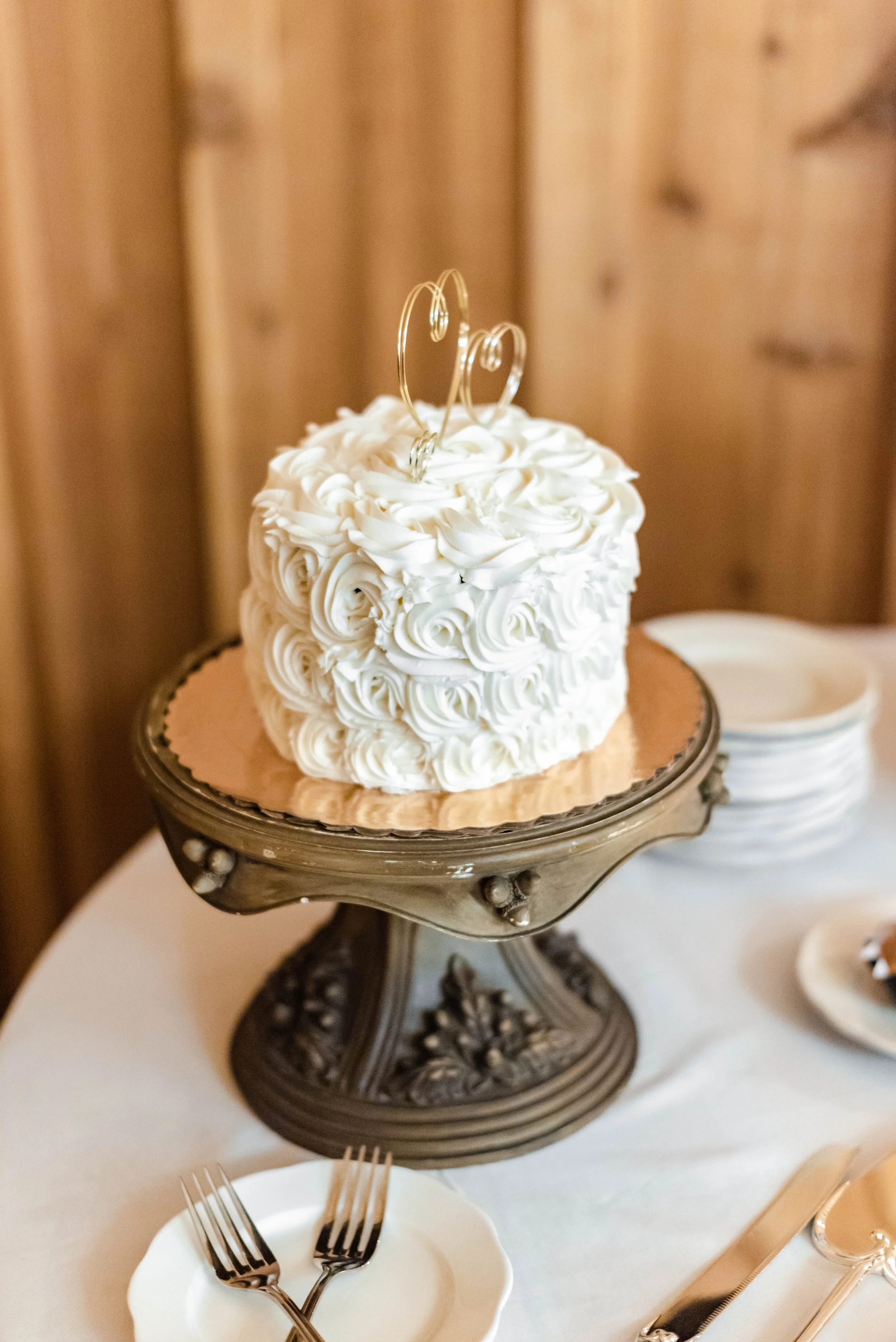 Small white rosette cake with a gold script cake topper on a vintage pedestal stand