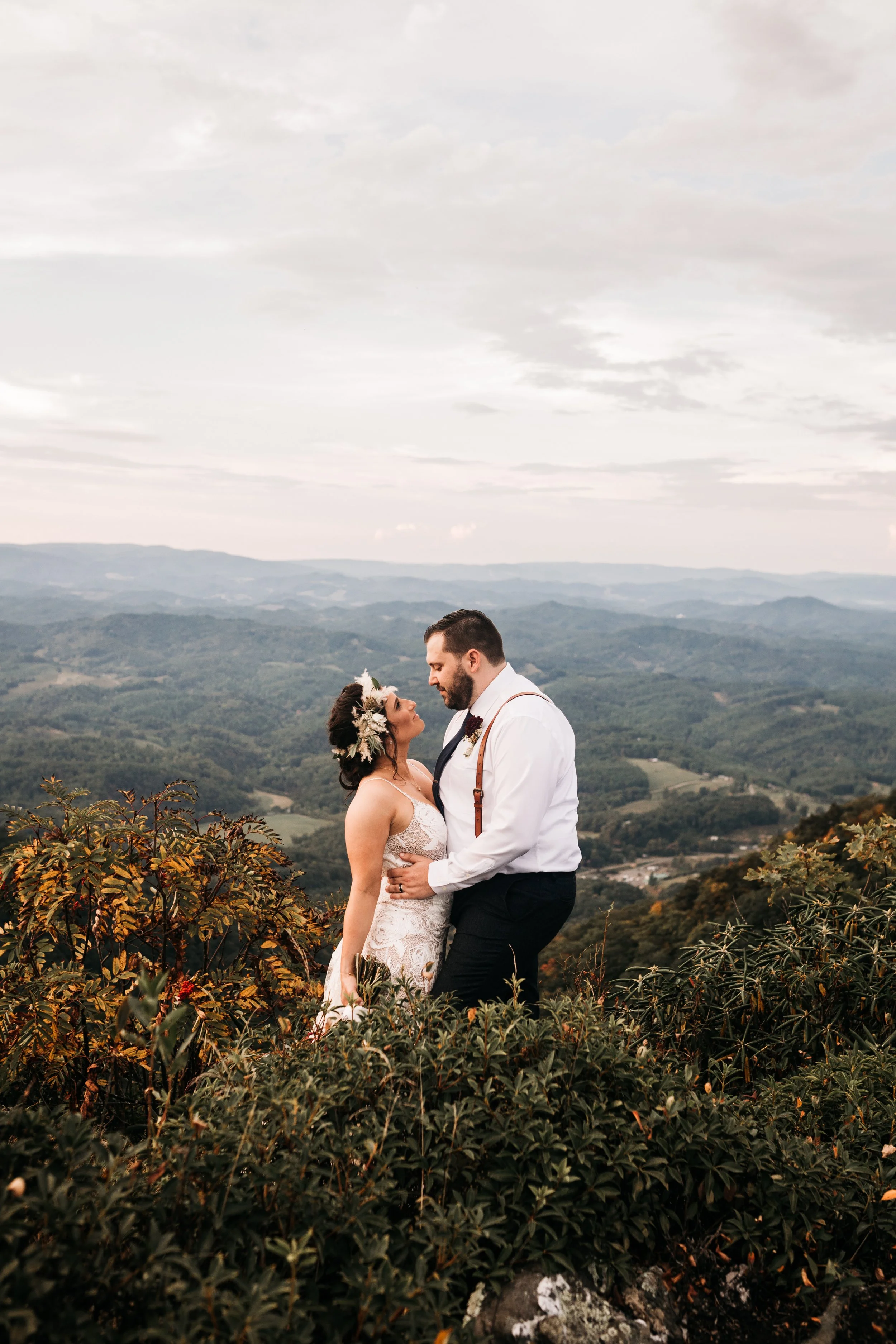 Bride and groom kissing with a panoramic mountain view and cloudy sky in the background.