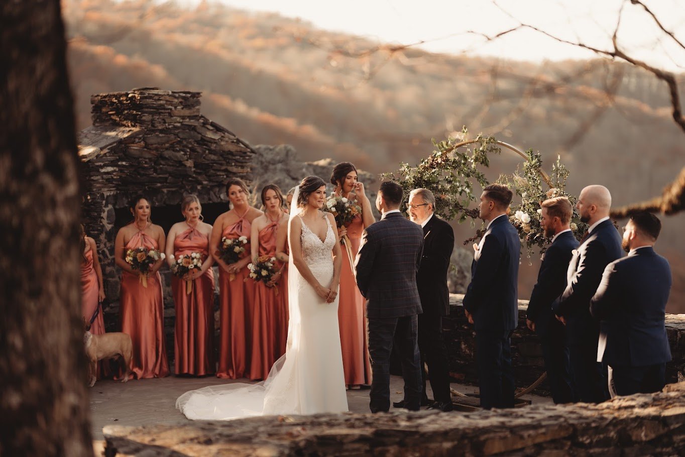 Wedding ceremony at sunset on a stone terrace with mountains in the background and the wedding party standing beside the couple