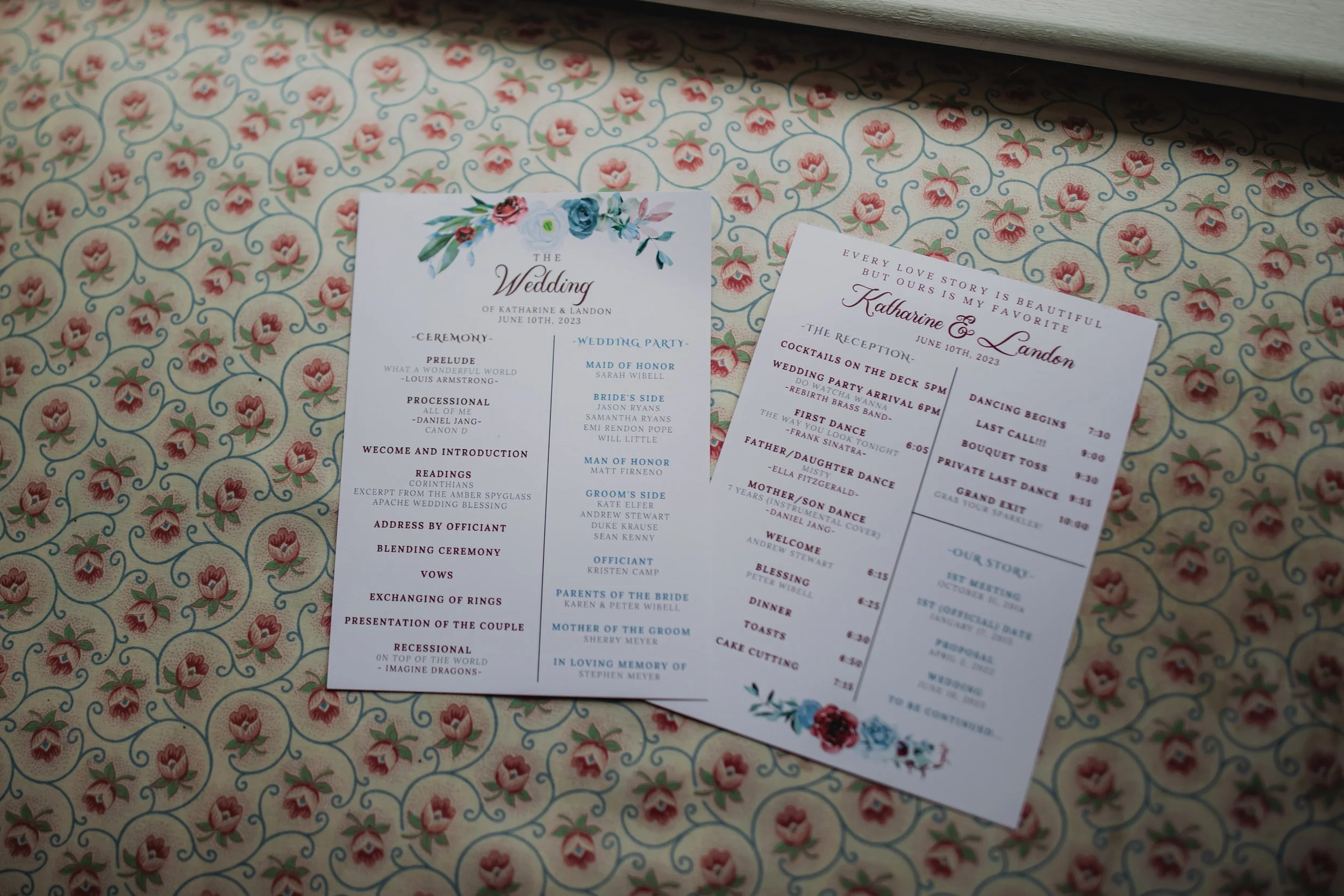 Printed wedding ceremony programs and reception schedule cards displayed on floral patterned wallpaper.