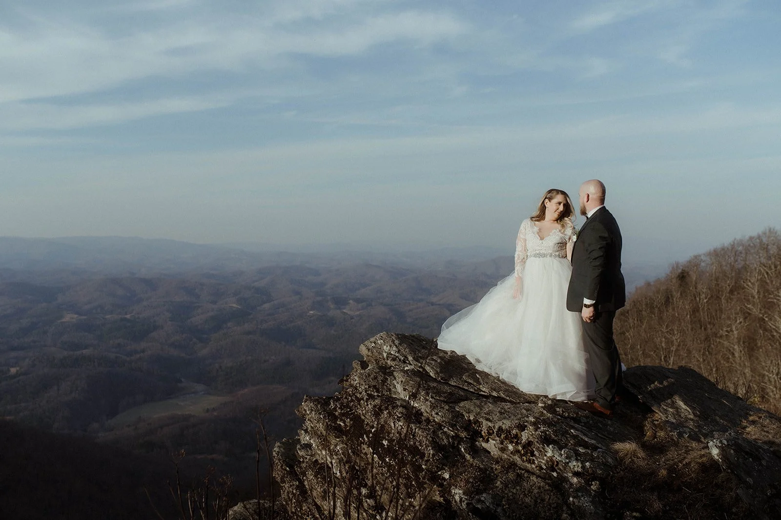 Bride and groom standing together on a rocky cliff with expansive mountain views