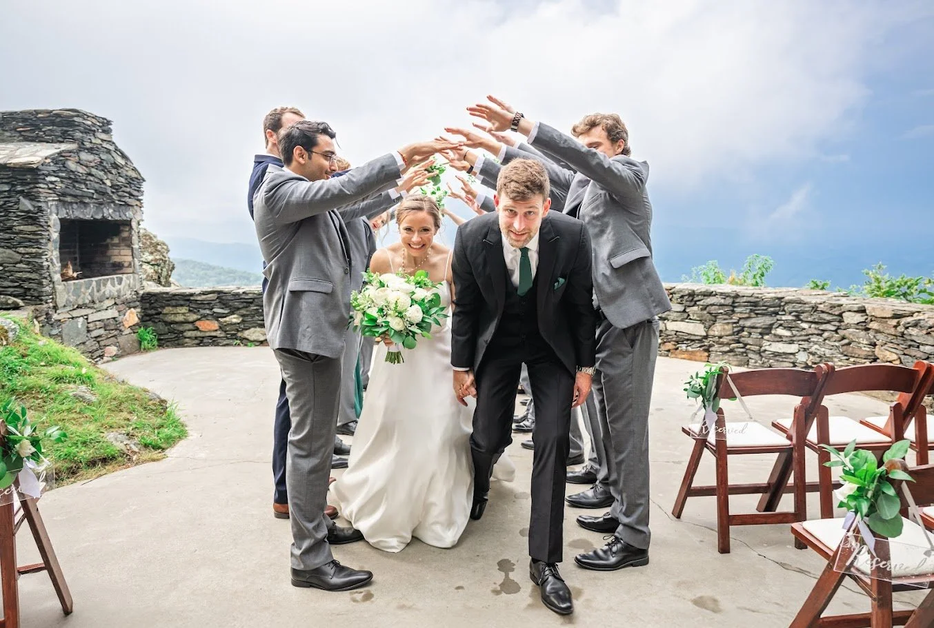Groomsmen forming a raised-arm tunnel as the bride and groom walk through after a mountain ceremony