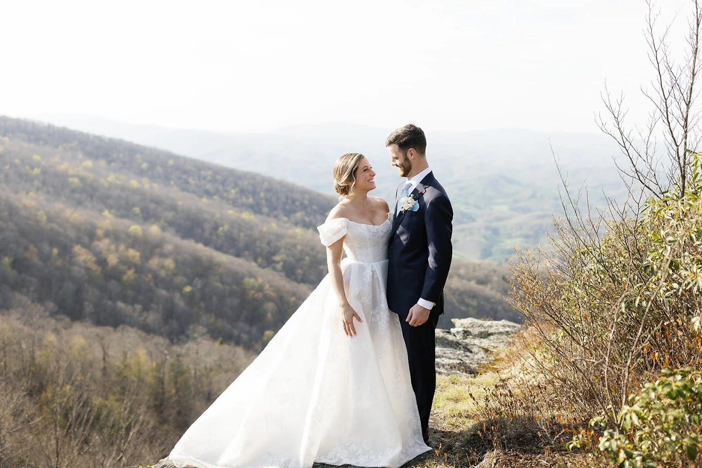 Bride and groom standing on a mountain overlook with layered mountain views in the background